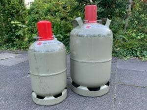 graue 5 und 11 kg Gasflaschen nebeneinander mit roten Deckeln